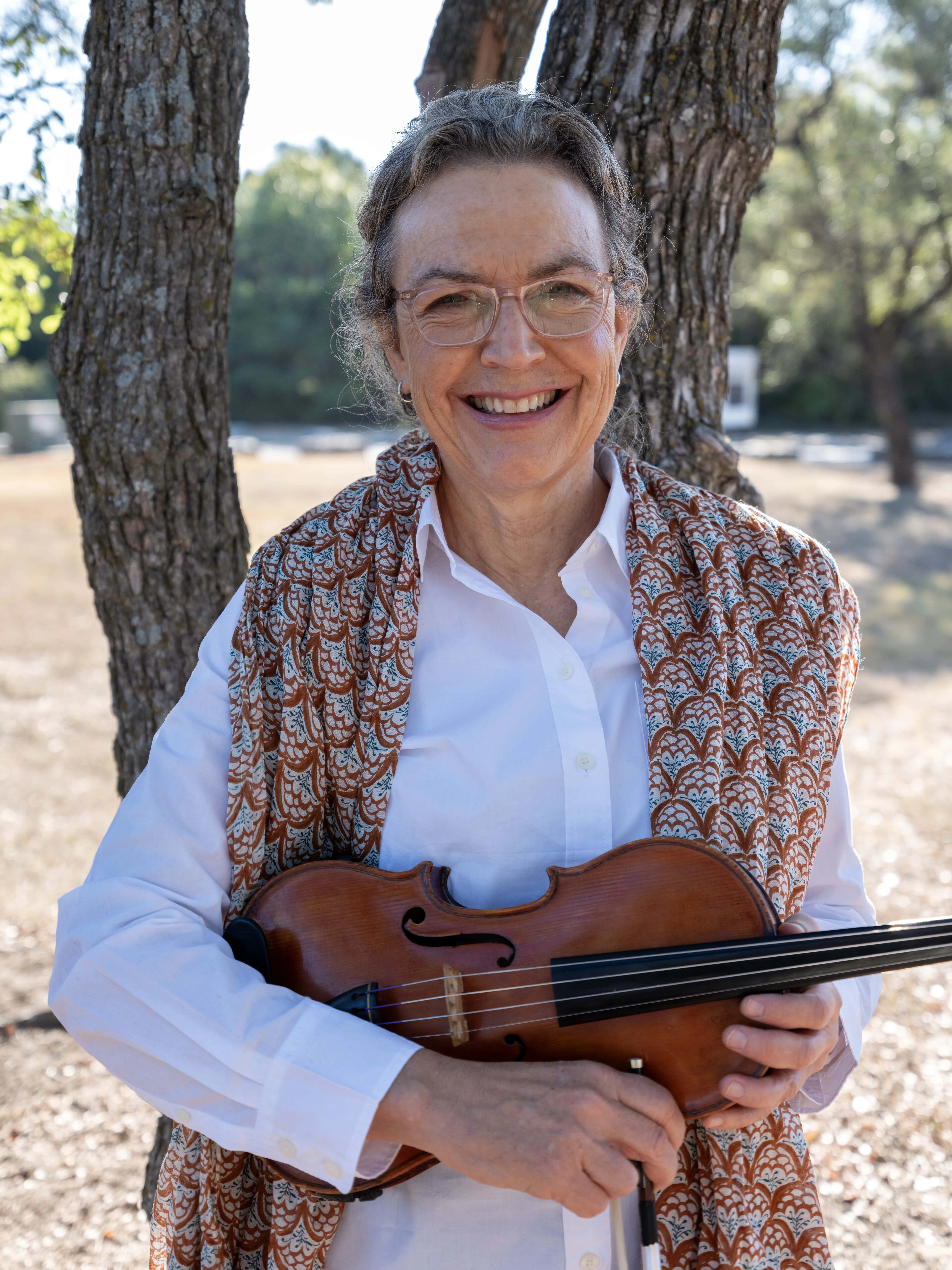 Jennifer Martens in white shirt and printed scarf holding her violin in rest position